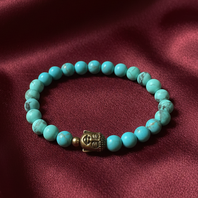 Turquoise beaded bracelet with a gold Buddha charm on a maroon fabric background